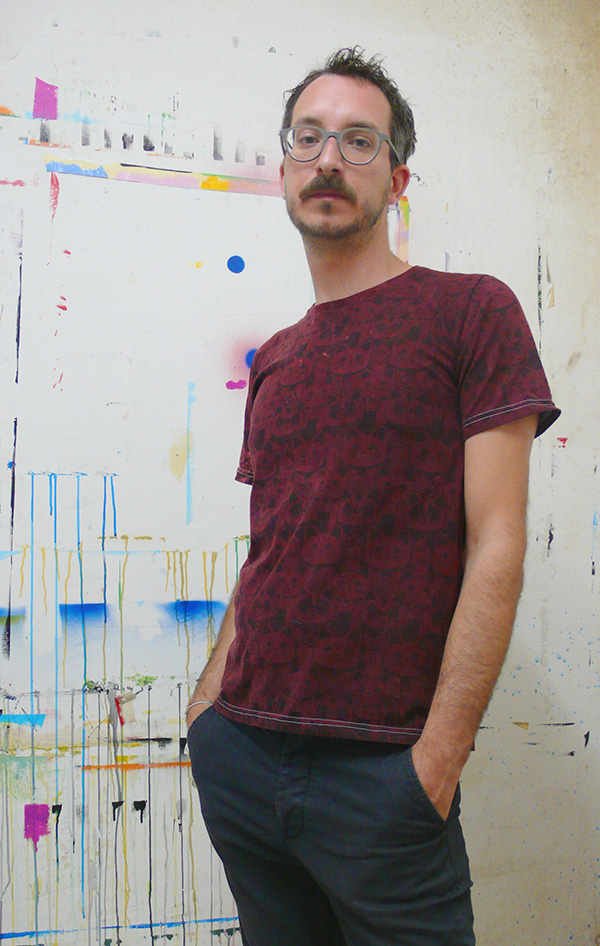 Giulio Zanet in his studio, stood against a paint-covered wall. 