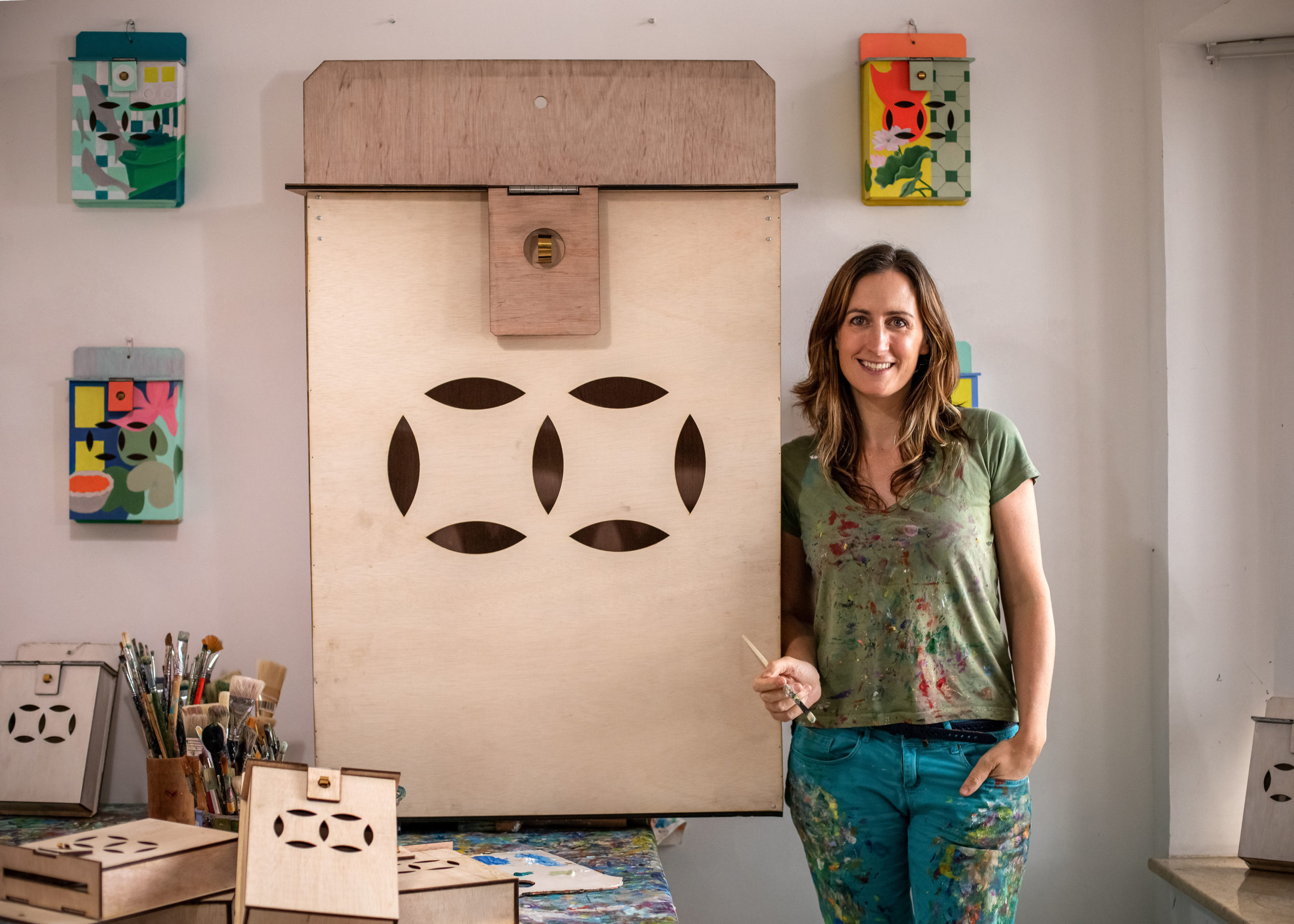 Eleanor McColl holding a painting brush, standing behind her large scale artwork of Mailboxes