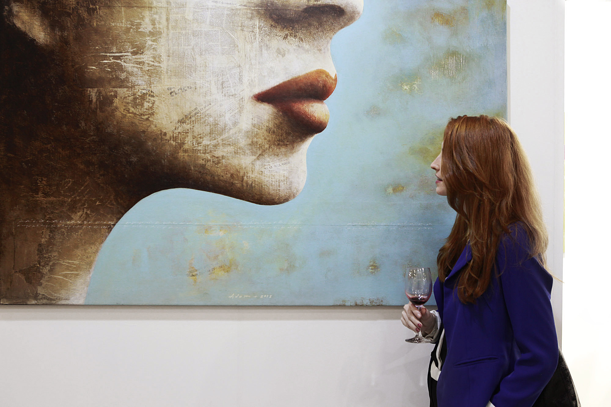 A women holding a glass of wine, stopping by an large painting hanging on wall