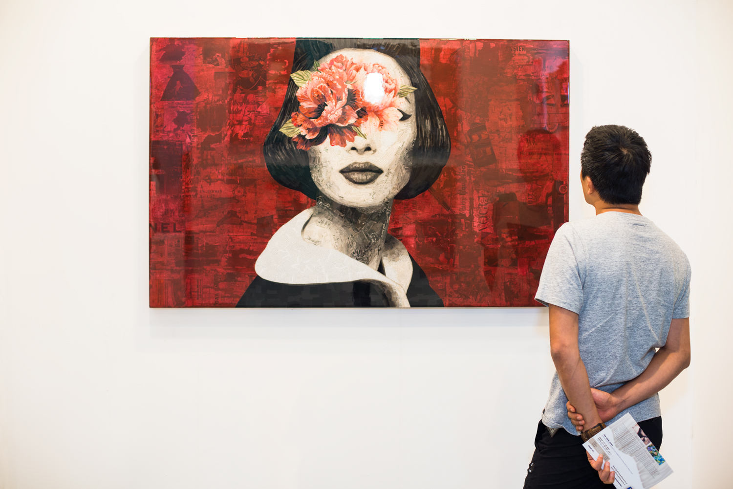 A man stopping by an artwork hanging on wall. Artwork of a female portrait with red color background.