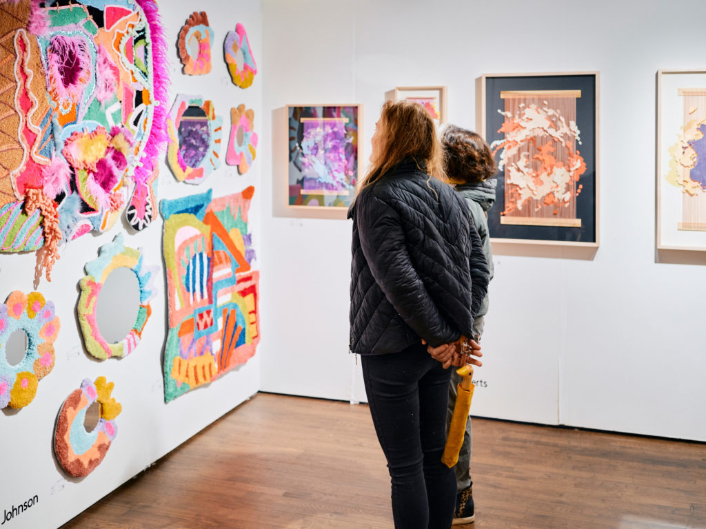 Image of two women staring at textured and colorful artworks hung by the NYC Spring Fellowship Gallery, Established Gallery