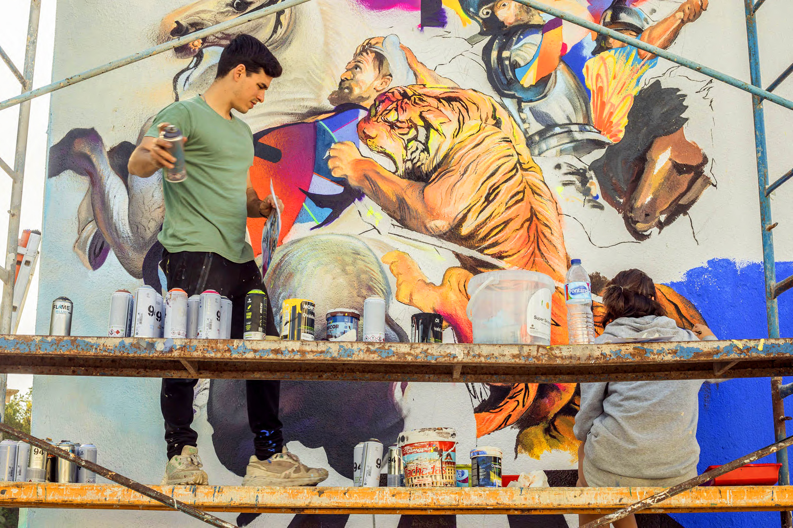 Murfin holding a spray can working on a mural painting, with a tiger roaring at the center