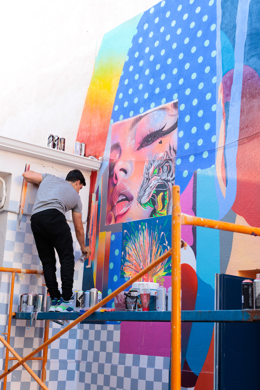 Murfin standing high on a stairs working on a colorful mural painting