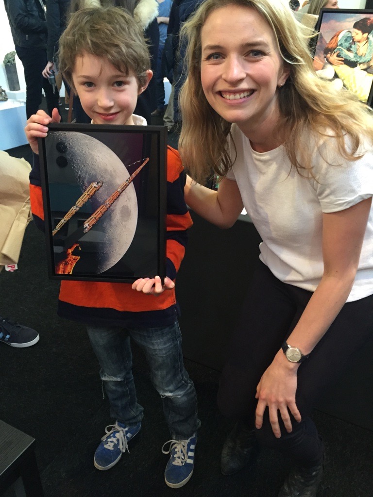 Blythe Bolton with a young art collector, who holds up his new purchase; an artwork of a moon with two spaceships. 