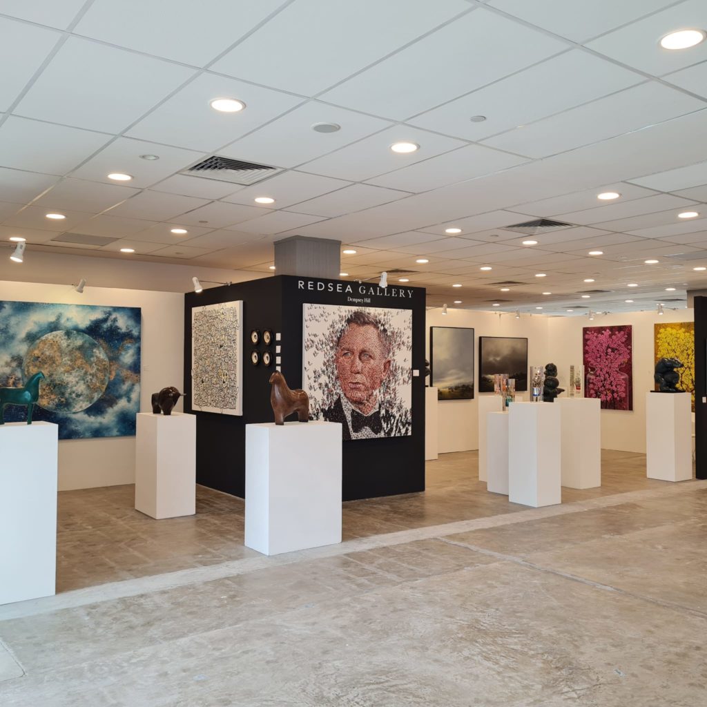 Inside an art gallery with large bright artworks on the walls and several plinths holding sculptures 