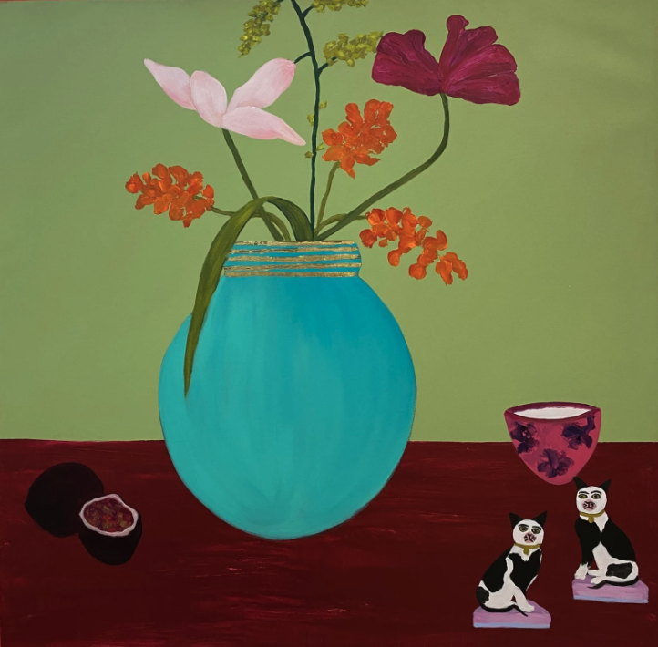 A dinner table scene. A blue vase holds five different flowers in red and pink hues. On the maroon table is a cut fig, bowl of cream and two miniature cat sculptures. 