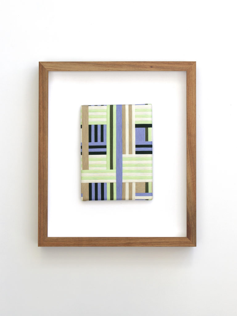 A framed artwork made from green and blue pastel threads woven together in a geometric form. 