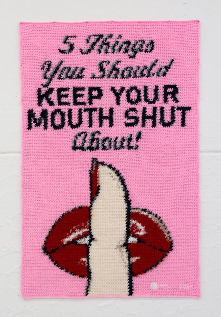 A crocheted tapestry in baby pink. A woman's finger is pressed to cartoon lips. Slanted vintage text reads: 5 things you should keep your mouth shut about! 