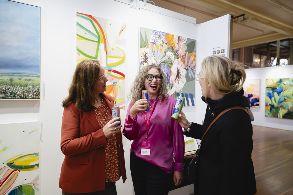 Group of smiling friends holding drinks at Affordable Art Fair.