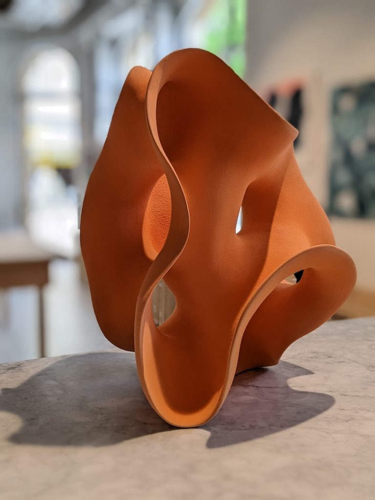 An orange clay sculpture placed on a kitchen countertop. The clay is formed into a flowing abstract shape. 