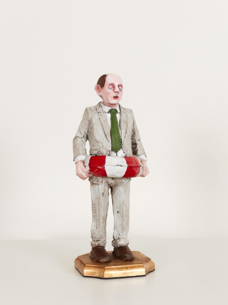 A miniature sculpture of a bald man in a grey suit with a rubber ring around his waist. 
