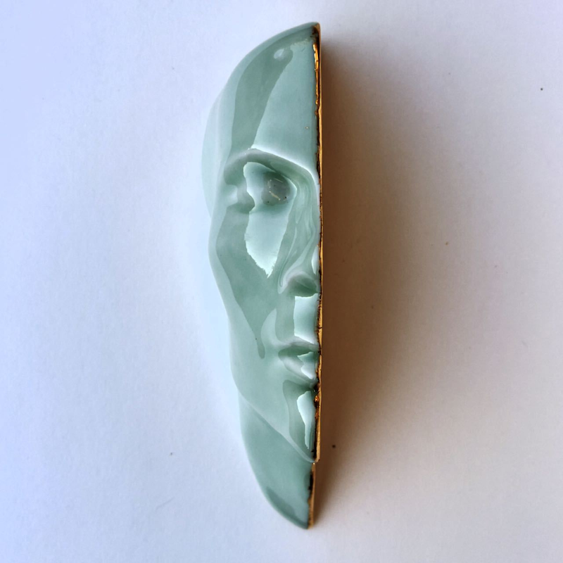 A light, duck egg blue sculpture of the left half of someone's face. The middle is plated with gold leaf.