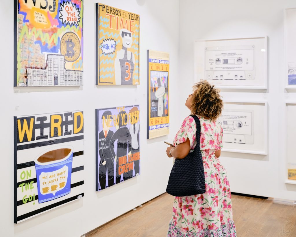 A woman staring up at a series of paintings depicting magazine covers